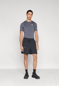 Γκρι αθλητική κοντομάνικη μπλούζα συνδυασμένη με μαύρο ρυθμιζόμενο σορτς και μαύρα αθλητικά παπούτσια, με λογότυπο στο πουκάμισο και στα σορτς.