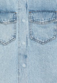 Svetlo modra denim srajca z dvema žepoma na prsih. Ima gumbasto zapiranje in belo šivanje. Tkanina ima mehak, strukturiran videz.
