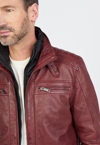 Rote Lederjacke mit strukturiertem Kragen, Reißverschluss auf der Vorderseite und zwei Brusttaschen. Mit schwarzer Innenauskleidung und strukturiertem Schulterdetail.