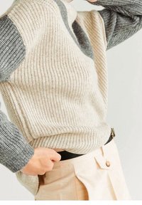 Sweter z prążkowanego dzianiny w beżowym kolorze z szarymi wstawkami na rękawach. Połączony z jasnymi, wysokim stanem spodniami ozdobionymi guzikiem.