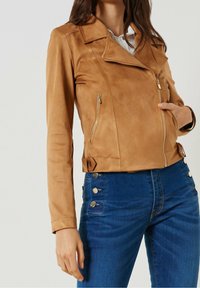 Tan faux kožená motorkářská bunda s přiléhavým střihem, asymetrickým zipem a dvěma zipovými kapsami. Tlačítkové akcenty na pase.