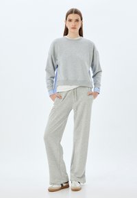 Sudadera de algodón gris con paneles laterales azules, combinada con pantalones de chándal grises a juego. Presenta un corte relajado y mangas con puños. Se incluyen zapatillas blancas.