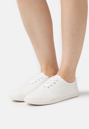 White canvas sneakers with round toe, six lace eyelets, and textured rubber sole. Minimal design and smooth finish.