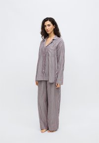 Conjunto de pijama a rayas grises y rosas con camiseta de manga larga abotonada y pantalones de corte holgado. Cuenta con un bolsillo en el pecho y textura de tela suave.