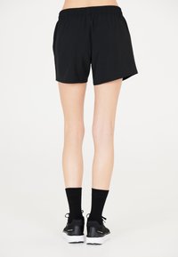 Svarta sportshorts med elastisk midja, slät textur, löst passform, tillsammans med svarta strumpor och sneakers. Bild tagen bakifrån.