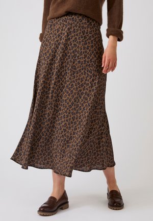 Bruine midi rok met luipaardprint, gedragen met een bruine trui en donkerbruine loafers op een staand model tegen een effen achtergrond.