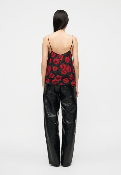 Μαύρο τοπ με λεπτές τιράντες και κόκκινο μοτίβο από τριαντάφυλλα, συνδυασμένο με μαύρο ψηλόμεσο παντελόνι από συνθετικό δέρμα με υφή.