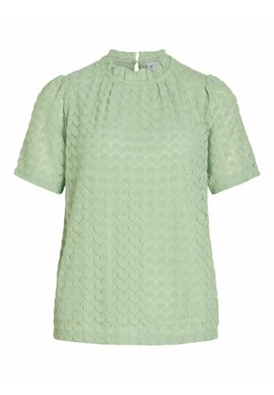 Lichtgroene blouse met korte mouwen en een gestructureerd patroon dat lijkt op schubben, met een ronde halslijn en een ritssluiting aan de achterkant.