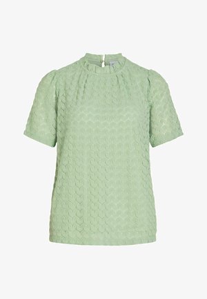 Heleroheline lühikeste varrukatega pluus, millel on soomuseid meenutav tekstuurimuster, ümar kaelus ja tagaküljel lukk.