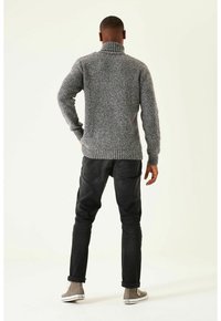 Pull à col roulé gris en maille, tissu texturé, ourlet et poignets côtelés, assorti à un jean foncé et des baskets grises, vu de dos.