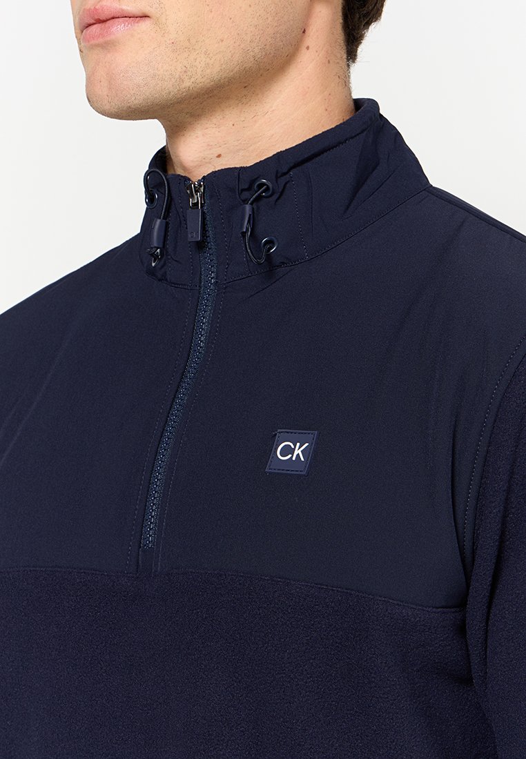 Marineblauwe half-zip pullover van gladde stof met een fleece onderstuk; beschikt over een trekkoordkraag en een CK logo patch.