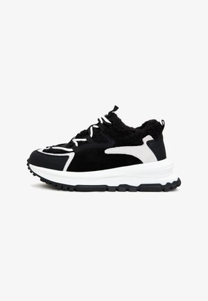 Černobílé tenisky s texturovaným černým svrškem, semišovými detaily a robustní bílou podrážkou s drsným černým vzorem. Nastavitelné tkaničky.