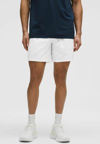 Conjunto masculino que presenta una camiseta sin mangas de textura en un azul marino oscuro y pantalones cortos blancos y ligeros. Zapatillas blancas con acentos claros y calcetines de canalé.