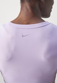 Back view of a person wearing a light purple Nike shirt with a small black Nike logo centered below the neckline.