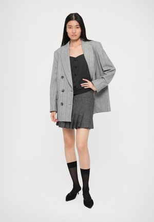 Gray double-breasted blazer over a black top, paired with a pleated black skirt and black knee-high socks, featuring pointed black heels.