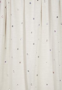 Beige Stoff mit texturierter Oberfläche, der gleichmäßig verteilte, schimmernde Pailletten aufweist, die der Oberfläche einen dezenten Glanz verleihen.