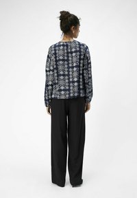 Blusa de color azul marino con estampado, de manga larga, fabricada en un tejido ligero, de corte holgado y con un escote redondo, combinada con pantalones negros de pierna ancha.