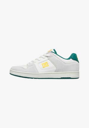Zapatilla blanca y gris con parte superior de ante y cuero, detalles verdes en el talón y la lengua, y logo amarillo. Suela de goma plana.