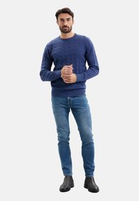 Maglione blu a trecce con scollo rotondo, abbinato a jeans azzurri e stivaletti neri. Focus sui dettagli di trama e motivo.