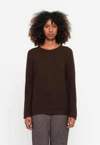 Brauner, gerippter Langarmpullover mit Rundhalsausschnitt. Der Stoff scheint weich zu sein, kombiniert mit strukturierten grauen Hosen.
