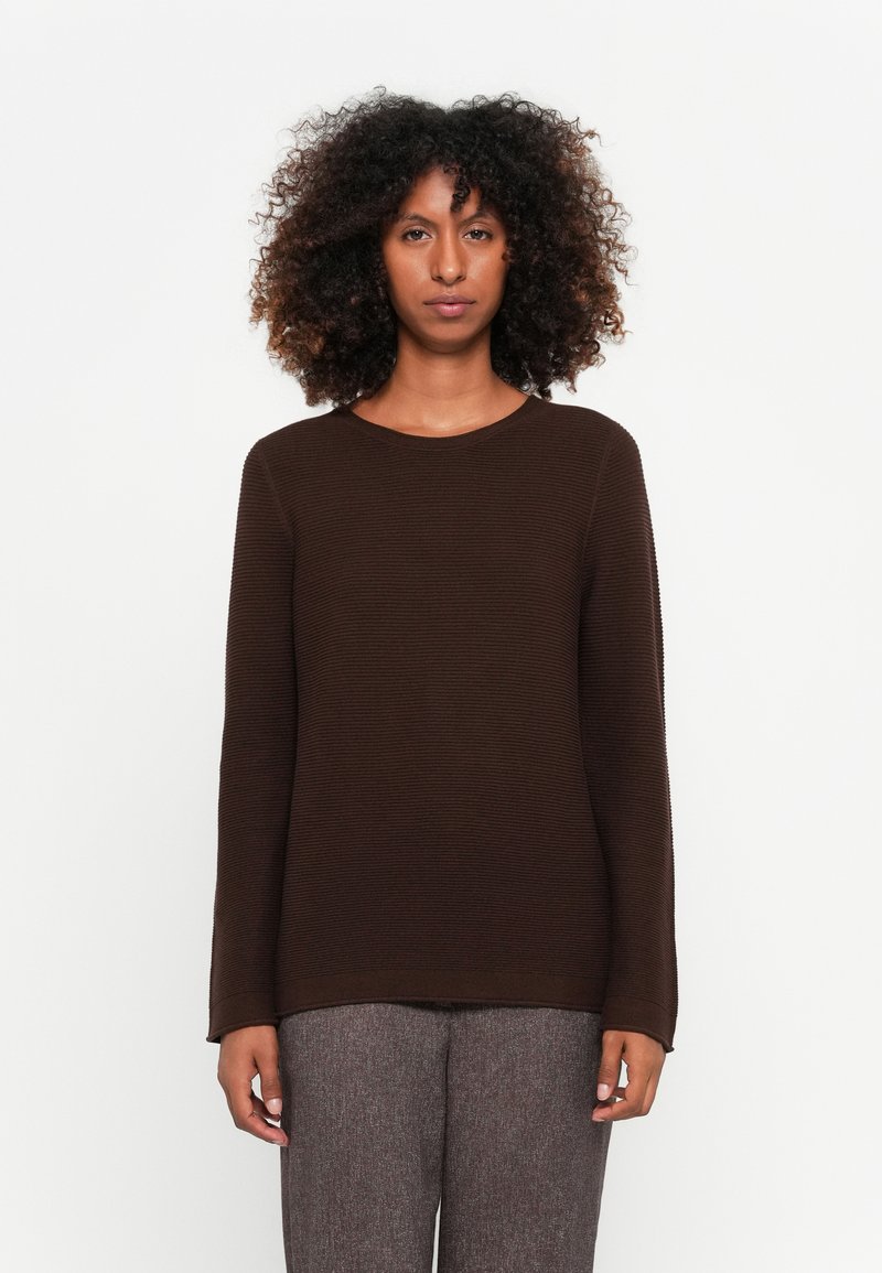 Brauner, gerippter Langarmpullover mit Rundhalsausschnitt. Der Stoff scheint weich zu sein, kombiniert mit strukturierten grauen Hosen.
