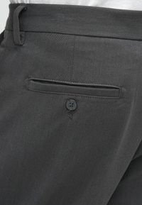 Pantaloni gri cu o textură netedă, având un buzunar pe spate prins cu un nasture negru și bucle pentru curea la talie.