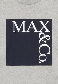 Šedé bavlněné tričko s velkým námořnickým obdélníkem s textem "MAX & Co." v bílé barvě, vertikálně zarovnaným na pravé straně.