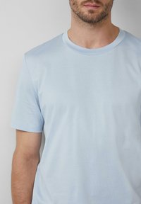 T-shirt in cotone azzurro chiaro con colletto rotondo e maniche corte, caratterizzato da una superficie liscia e una vestibilità attillata. Nessun motivo o dettaglio visibile.