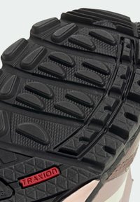 Suela de zapato de goma negra con patrones de agarre texturizados, detalle rojo "TRAXION" y acentos laterales en beige y blanco. Diseño duradero para tracción.