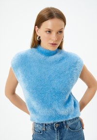 Blå, fluffig tröja med hög krage och korta ärmar, med ribbad textur. Parad med höga blåjeans.