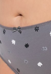 Grijze katoenen slips met een patroon van kleine zwarte, witte en grijze bloemen. Afgewerkt met een delicate rand en een strikaccent.
