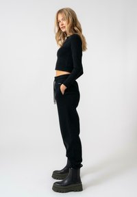 Top cropped nero a maniche lunghe abbinato a pantaloni jogger neri con vita elastica e tasche, indossato con stivaletti alla caviglia neri con plateau.