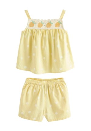 Żółty bezrękawnik w groszki z haftowanym owocowym wykończeniem, do kompletu pasujące szorty na elastycznej talii w jasnym żółtym kolorze z białymi kropkami.