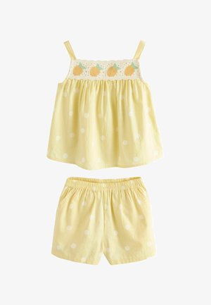 Sárga pöttyös ujjatlan felső hímzett gyümölcsdísszel, világos sárga, fehér pöttyökkel díszített, rugalmas derékpántos rövidnadrággal párosítva.