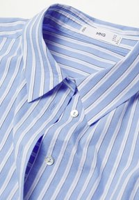 Light blue button-up shirt with white horizontal stripes. Features a fold-down collar and textured fabric. Includes a small white button.
