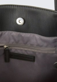 Pelēka auduma roku soma iekšpuse ar melnu ribotu oderi, sudraba pogu aizdari un somiņu ar rāvējslēdzēju, kurai ir birka ar uzrakstu "DENIM TOM TAILOR."