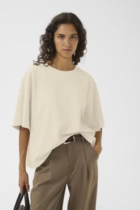 Avslappet passform, kremfarget t-skjorte med rund hals og korte ermer, kombinert med høyt liv, brune bukser. Myk tekstur, minimalistisk design.