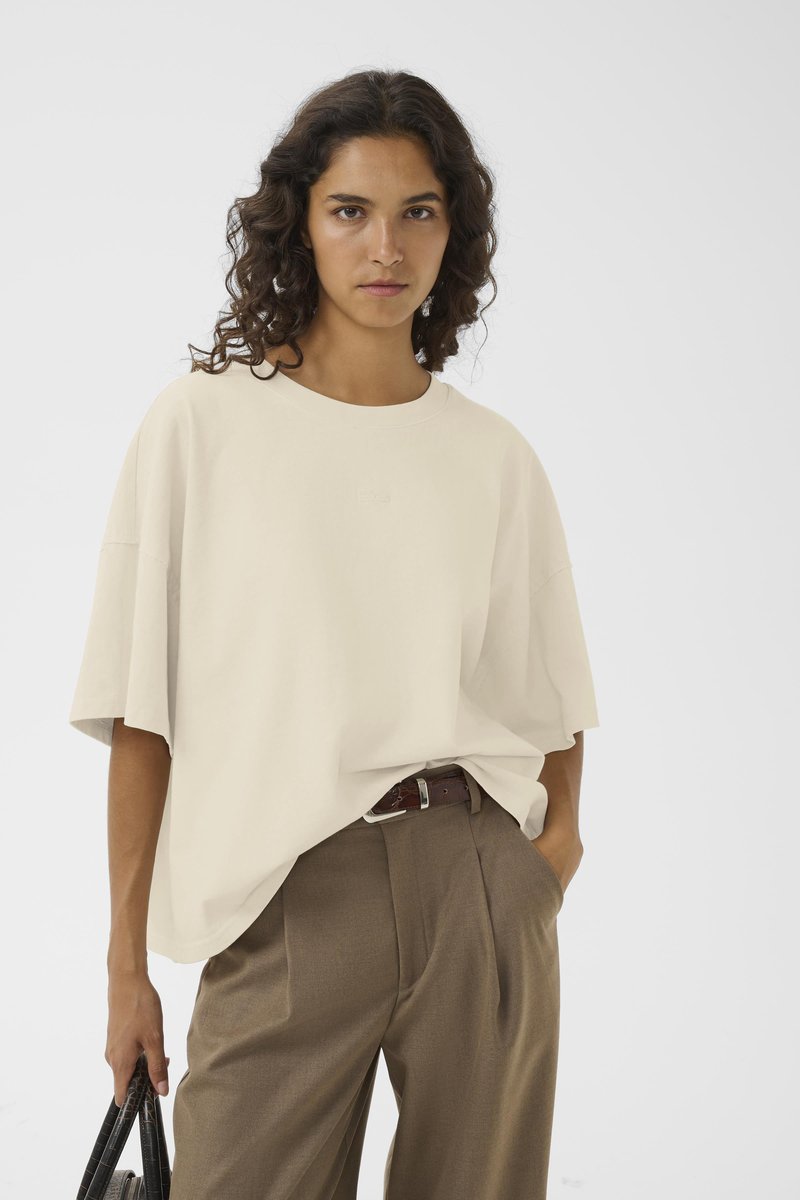 Avslappet passform, kremfarget t-skjorte med rund hals og korte ermer, kombinert med høyt liv, brune bukser. Myk tekstur, minimalistisk design.