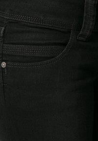 Jeans de mezclilla negra con una textura suave, que cuentan con un bolsillo delantero curvado, costuras tonales y un acento de botón de metal plateado.