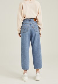 Vaaleansiniset korkeavyötäröiset farkut, joissa on löysä leikkaus, kaksi takataskua, nahkainen tuotemerkki ja hienovaraisesti rispaantunut helma.