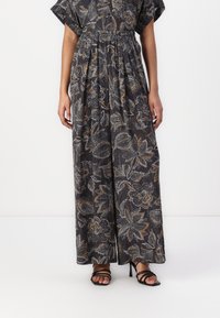 Maxi-jurk van donkere stof met een bloemmotief in crèmekleur, oranje en grijs. Voorzien van losse mouwen en een elastische taille. Gepaard met zwarte hoge sandalen.
