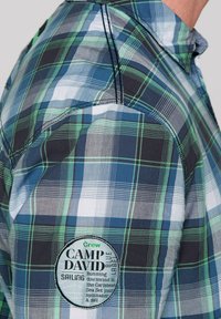Camicia a quadri con check blu, verde e grigio, con un logo ricamato rotondo che riporta "Camp David" sulla spalla sinistra.