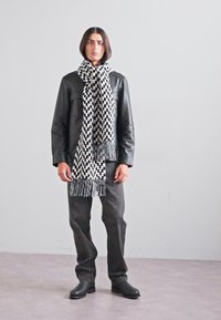 Black and white patterned scarf with fringe, layered over a black leather jacket. Dark grey pants and black boots complete the outfit.