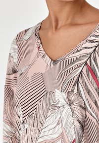Kurzärmlige Bluse aus weichem pinkfarbenem Stoff mit einem V-Ausschnitt, aufwendigen botanischen Illustrationen und diagonalen gestreiften Mustern in Schwarz und Weiß.