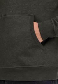 Hand partially inserted into a front pocket of a dark gray sweatshirt with visible stitching and ribbed cuff.