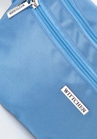 Modrá látková taška s texturovaným povrchem, vybavená stříbrným zipem a bílou štítkem s logem "WITTCHEN." Obdélníkový tvar.