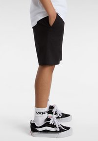 Pantaloni corti neri con tasche laterali, indossati con calze bianche e sneakers nere con accenti bianchi. Design semplice, materiale in cotone.