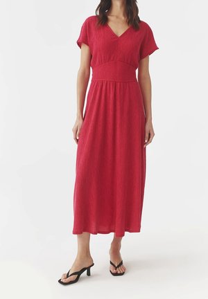 Czerwona sukienka midi z dekoltem w kształcie litery V i krótkimi rękawami. Materiał o fakturze, z dopasowanym gorsetem i zwiewną spódnicą. Noszona z czarnymi klapkami.