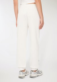 Białe dresy z luźnym krojem, elastycznym pasem i przylegającymi kostkami. W połączeniu z srebrnymi trampkami o teksturowanym wzorze.