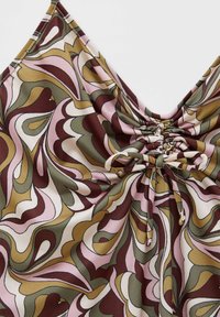 Gros plan d'un haut sans manches avec devant froncé et lien, présentant un motif abstrait tourbillonnant en tons vert olive, marron, rose et beige.